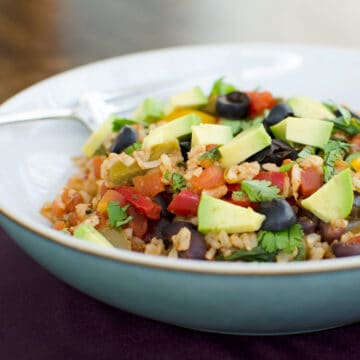 bowl of rice and beans topped with avocado, black olives, and cilantro