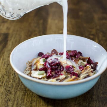 plant milk being poured over old-fashioned oats mixture with dried fruits and seeds