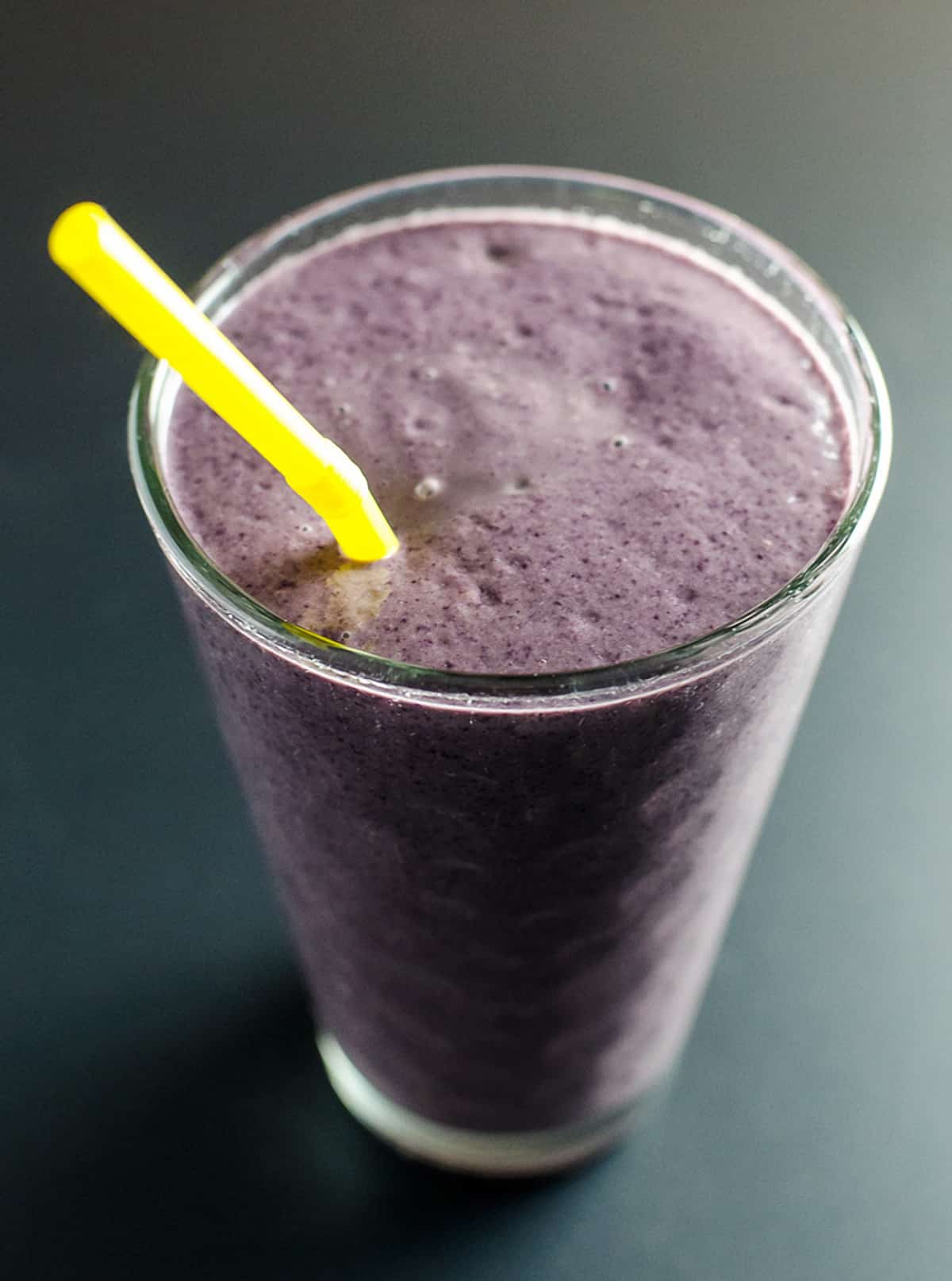 Purple super food smoothie in a tall glass with a yellow straw